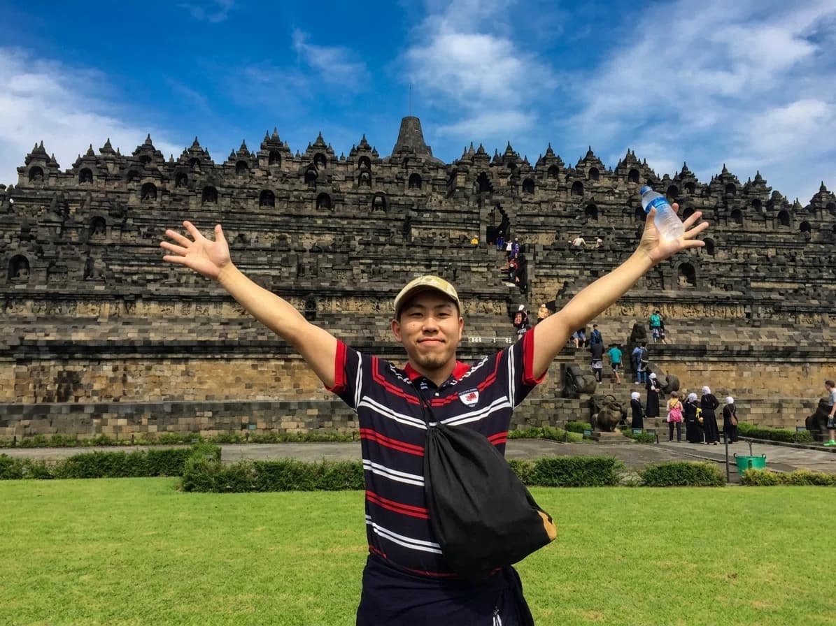 A Puri Bahasa student posing with arms raised in front of Borobudur temple