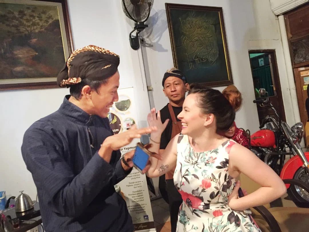 A Puri Bahasa student chatting with a Javanese man in traditional blangkon headwear